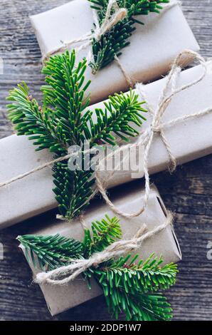 Modern Christmas wrapped presents with natural decoration on old wooden background. Three gifts boxes in craft paper with twine and green branches. Se Stock Photo