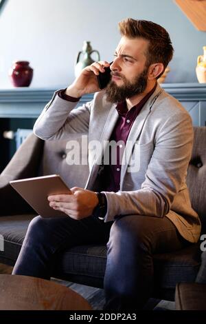 Portrait of young pensive businessman talking on cell phone in office Stock Photo