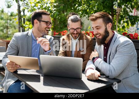 Positive successful business specialists discussing plan with laptop outdoors. Stock Photo