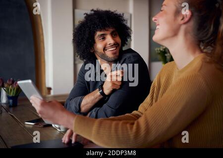 Cheerful man and woman laughing and talking in cafe using digital tablet Stock Photo