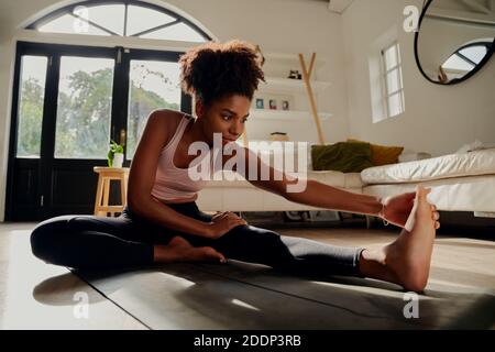 Slim sportswoman in sportswear warming-up muscles before workout doing stretching exercise sitting on floor at home Stock Photo