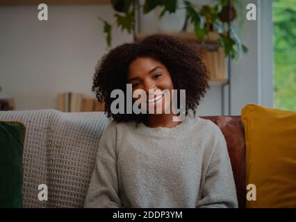 Portrait of beautiful woman with curly hair and toothy smile sitting on sofa at home Stock Photo