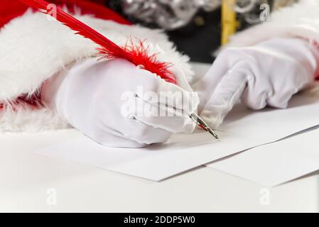 Costumed hands of Santa Claus writing a Christmas letter or greeting on a postcard. close up Stock Photo