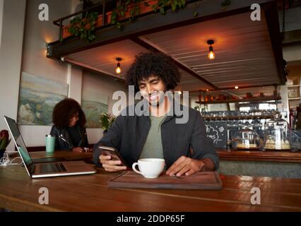 Handsome young man using smartphone and laptop in modern cafe while drinking coffee Stock Photo