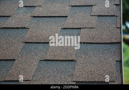 A close-up a roof covered with copper brown bitumen, asphalt laminated, dimensional, or architectural roofing shingles.  Asphalt shingles background. Stock Photo