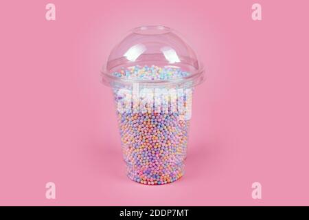 Takeaway plastic cup with dome for cold drinks filled with colorful sugar balls on pink background. Rainbow colored candies, sweet holidays concept Stock Photo