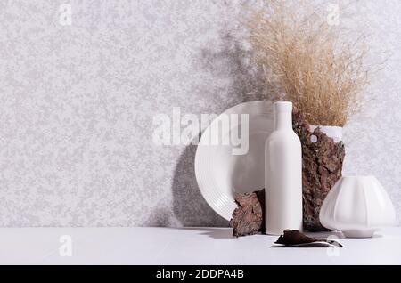 Scandinavian minimalist interior with ceramic vase, dish, dried grass bouquet, brown tree bark, moss in sun beam with shadow on white wood table. Stock Photo
