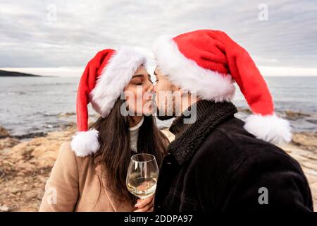 Passionate kiss of lover couple on sea rocks in winter sea Christmas and New Year vacation - Young beautiful girlfriend and boyfriend bonding wearing Stock Photo