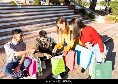 Two couple of friends sitting on city square steps checking their purchases in colored shopping bags - Winter young satisfied customers happy with wha Stock Photo
