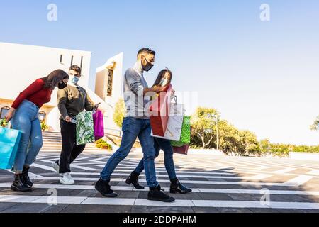 Young friends group outdoor in the city square walking satisfied of purchases wearing Coronavirus safe protection mask - Beautiful people with casual Stock Photo
