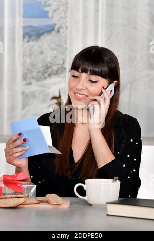 Beautiful young woman enjoying a talk on her phone while reading a letter - gifts receiving Stock Photo