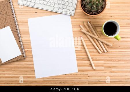 Designer’s wooden desk with computer keyboard, coffee cup, cactus,  stationery, color pencils  and copy space on blank paper Stock Photo