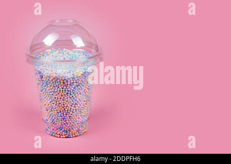 Takeaway plastic cup with dome for cold drinks filled with colorful sugar balls on pink background. Rainbow colored candies, sweet holidays concept Stock Photo