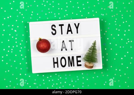 Light box with text STAY AT HOME and Christmas decoration on green background. Top view Stock Photo