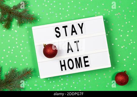 Light box with text STAY AT HOME and Christmas decoration on green background. Top view Stock Photo