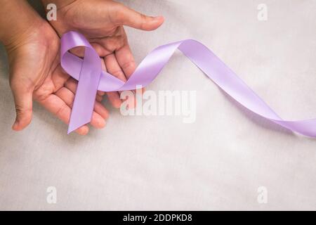 Hands holding light purple ribbon on white fabric with copy space. Testicular Cancer Awareness, Alzheimer disease, Epilepsy awareness, World Cancer Da Stock Photo