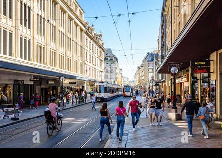 Couples, families and friends strolling in the main shopping street in Geneva, served by tramway and trolleybus, on a sunny summer day. Stock Photo