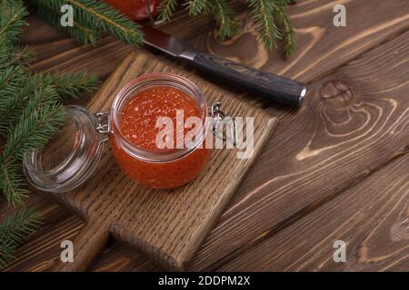Red caviar in a glass jar on a seasoned white wooden background with a Christmas tree. Stock Photo