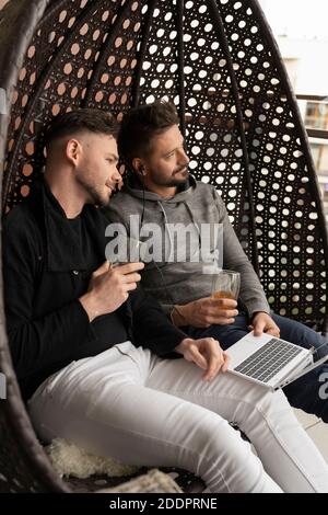 European Gay lgbtq men drinking beer and using laptop on the balcony. High quality photo Stock Photo