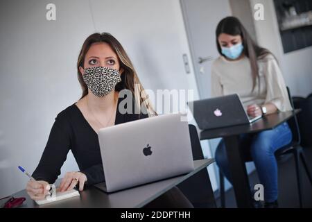 Themed picture CoWorking Space. Two young women sit at individual tables and wear face masks and masks. You are working on your laptop in a CoWorking office on November 22nd, 2020. Alternative to home office. Coworking is a development in the area of 'new forms of work'. Freelancers, smaller startups or digital nomads work in mostly larger, relatively open spaces and can thus benefit from each other. You either work independently in different companies and projects or develop projects together with other coworkers. MODEL RELEASED! | usage worldwide Stock Photo