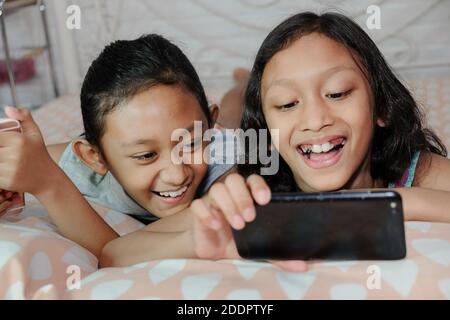 Southeast Asian ethnicity teenage girls siblings together having fun viewing information from social media through smartphone Stock Photo