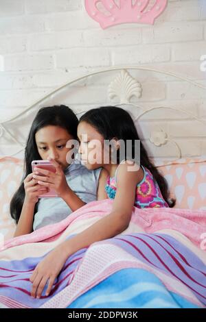 Southeast Asian ethnicity teenage girls siblings together curiously viewing information from social media through smartphone Stock Photo