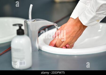 Close up of male hands being rinsed at a bathroom sink on an out of focus background. Hygiene and safety concept. Stock Photo