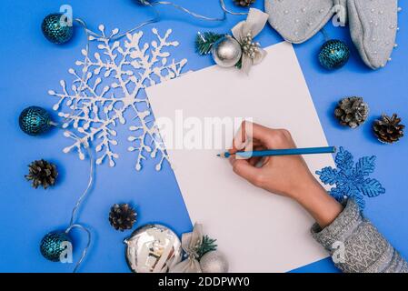 The girl writes on a white sheet of paper. Christmas greeting card. Composition of New Year's toys, garlands, snowflakes and cones. Winter, Christmas Stock Photo