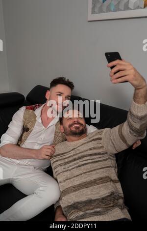 Homosexual relationship concept. Romantic gay couple relaxing on the couch. Boyfriends taking selfie with smartphone. High quality photo Stock Photo