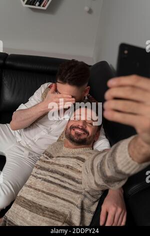 Romantic gay couple using smartphone for video call. One of the boyfriends hiding his face with the hand. Shy partner . High quality photo Stock Photo