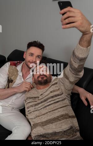 Homosexual relationship concept. Romantic gay couple relaxing on the couch. Boyfriends taking selfie with smartphone. High quality photo Stock Photo