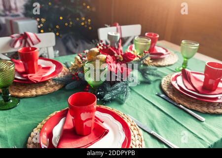 Beautiful festive holiday xmas family table setting served for 4 persons with light, christmas tree and many gifts on background. Simple warm rustic Stock Photo