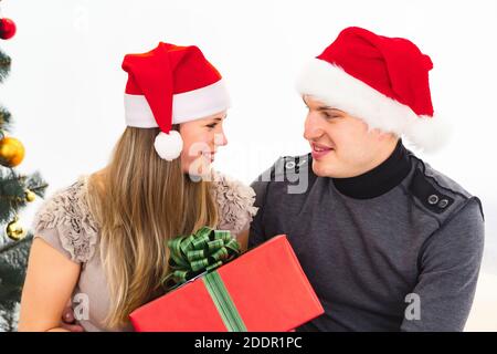 Young couple in christmas santa hats giving a gift isolated on white background Stock Photo