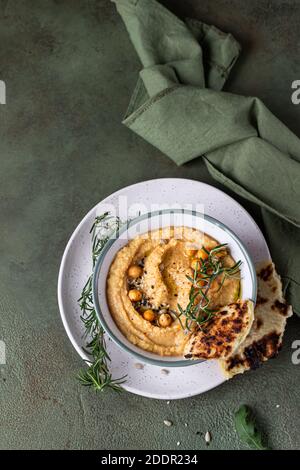 Classic hummus with rosemary, flatbread, boiled chickpea and olive oil, green stone background. Traditional Middle Eastern snack. Top view. Stock Photo