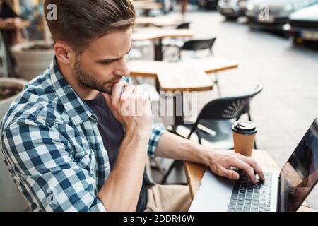 Happy young man working on laptop computer while sitting at sidewalk cafe Stock Photo