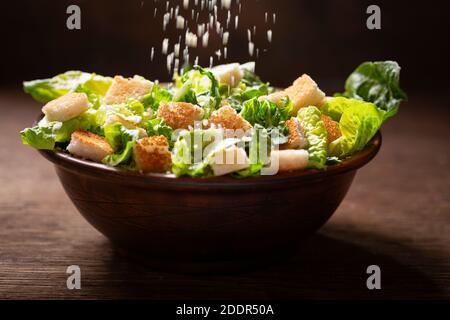 Falling cheese into Bowl of fresh caesar salad on a wooden table Stock Photo