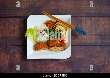 Japanese salmon fish cake, rice, noodle salad and vegetables on a white plate. Rustic dark wooden table background. Stock Photo