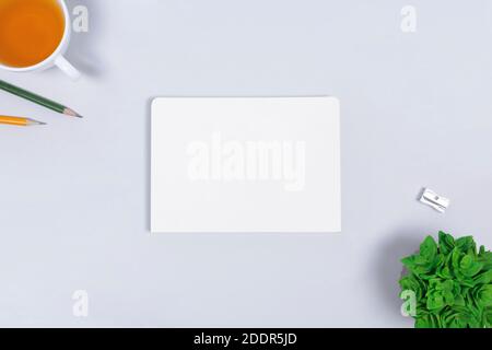 Workplace with blank paper notepad, cup of tea, pencils, sharpener, succulent on light gray backgroud. Office table desk. Flat lay with copy space Stock Photo