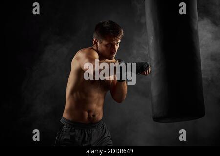 Male boxer training defense and attacks in boxing bag on black background with smoke Stock Photo