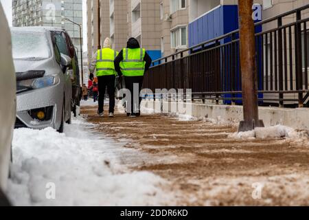 Two workers in yellow reflective vests sprinkle sand on a walkway from a cart. Stock Photo