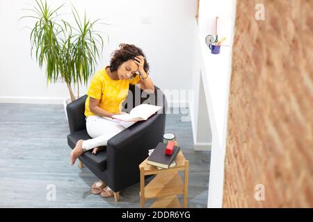 Top view of a latin woman focused on reading a book at home. Space for text. Stock Photo