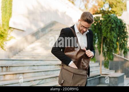 Handsome unshaven businessman in earphones walking down stairs on city street Stock Photo