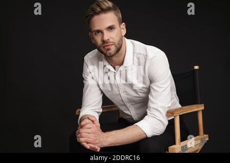 Handsome confident businessman sitting in armchair isolated over black background Stock Photo
