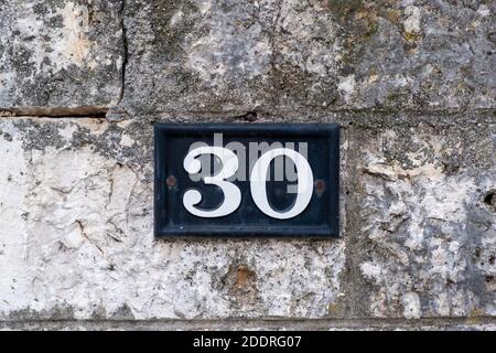 Street number thirty. Digit 30 white color on metal vintage plate mounted on stone wall. Traditional house address Stock Photo