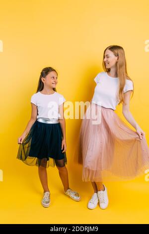 A beautiful young woman with her little charming daughter look lovingly at each other on an isolated yellow background Stock Photo