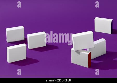 Seven small white carton boxes or packs with colorful sides and no logo against purple studio background. Close up, copy space Stock Photo