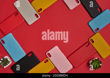 Set of colorful protective cellphone cases and two green succulents in pots on red studio background. Close up, copy space. Top view, flat lay Stock Photo