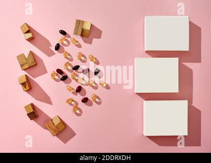 Three small cardboard boxes with no logo, scattered colorful capsules and wooden blocks of different shapes on pink background. Close up, copy space Stock Photo