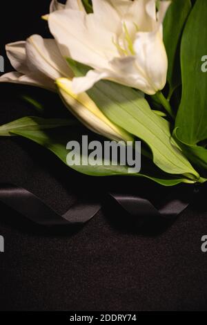 closeup of lily bouquet and ribbon on black background, funeral concept Stock Photo