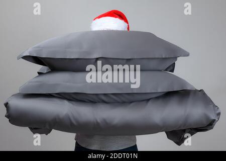 Woman in Santa Claus hat holding a warm duvet and feather pillows of gray. Bedding for sleeping. Stock Photo